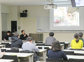 会場前方のスクリーンに映したまちづくりの取組の写真について講師が紹介している様子。